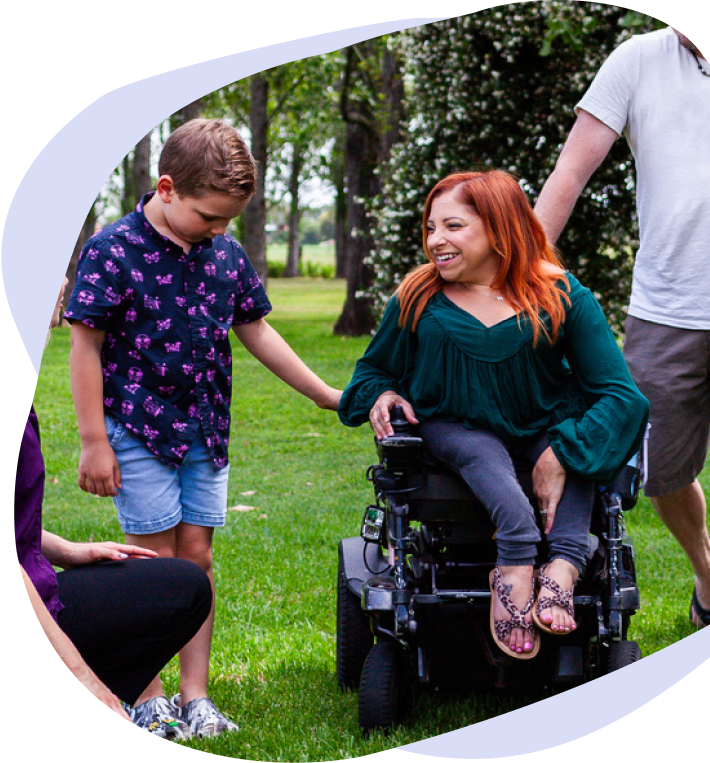 A smiling woman in a wheelchair with her family and a therapist
