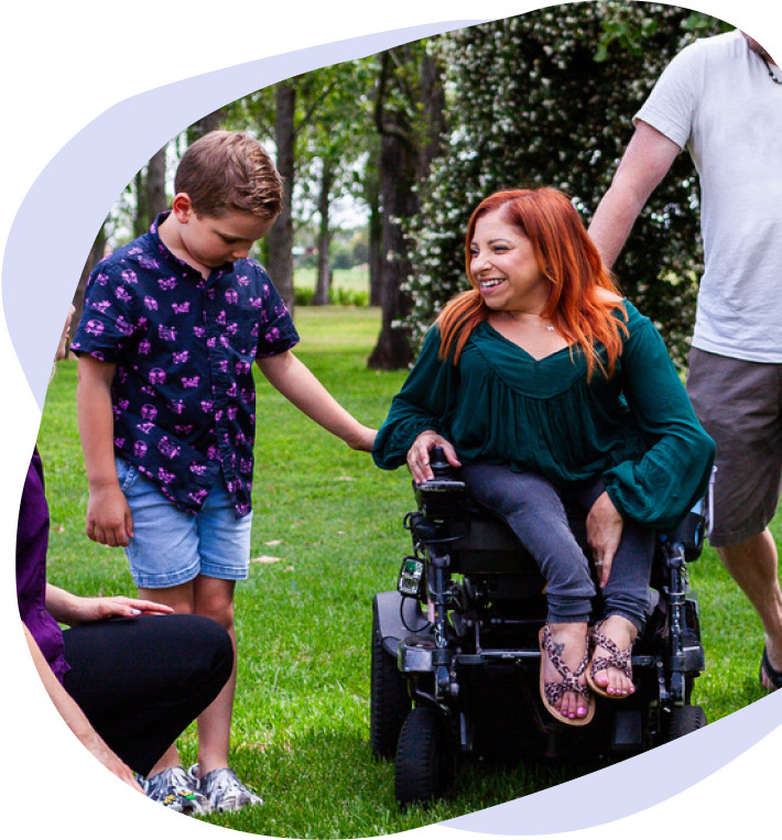 A smiling woman in a wheelchair with her family and a therapist