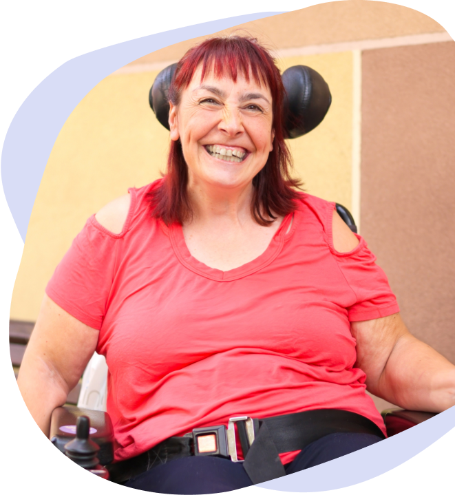 A woman with an aquired brain injury is smiling whilst sitting in a wheelchair