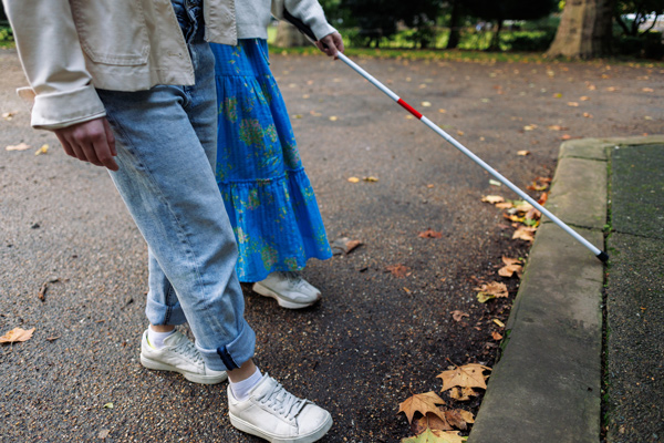 Person walking with a cane to guide them accompanied by a support worker
