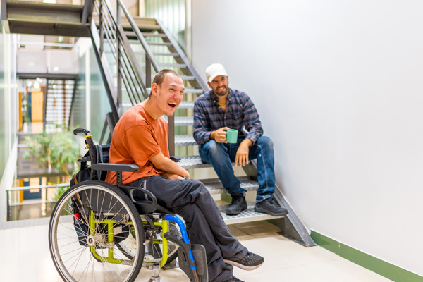 A smiling young man with cerebral palsy sits talking to his support worker