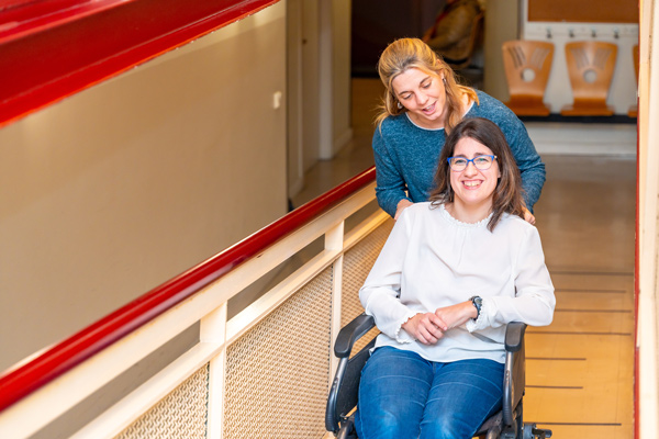 A woman sits in a wheelchair smiling at her support worker