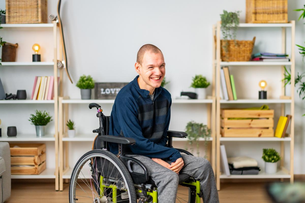 Young man seated in wheelchair in his home in front of shelf