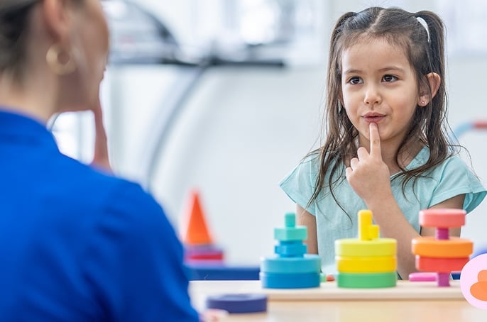 Young girl in a speech therapy session with her finger on her lips