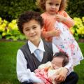 Maia as a newborn baby in the arms of her brother with her sister standing behind him