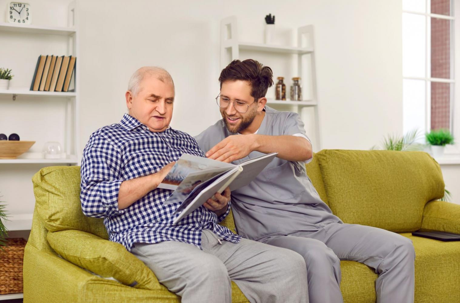 Gentleman with carer seated on a couch reading a book