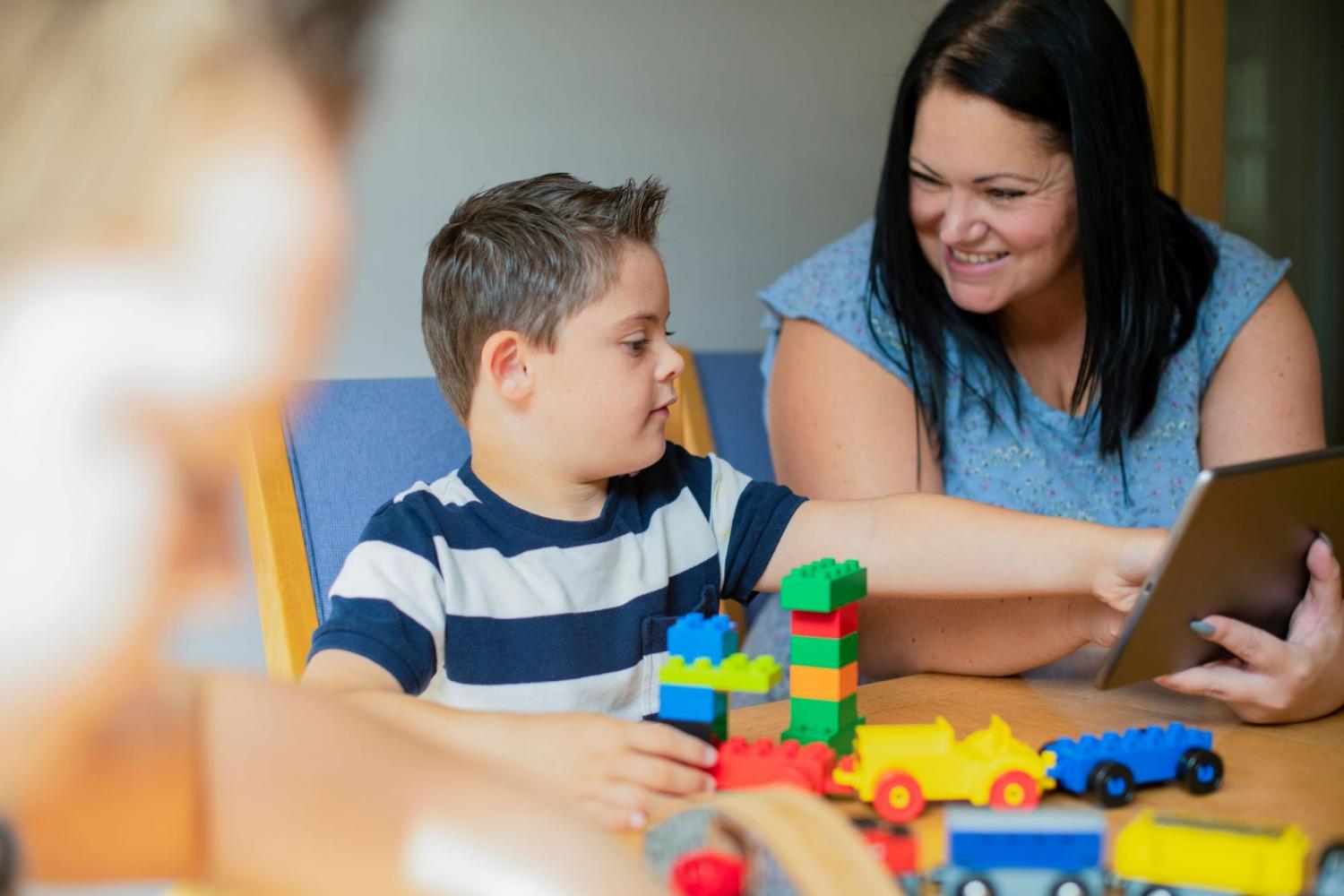 Child learning with therapist using ipad and lego set