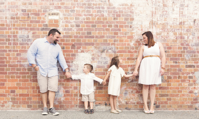 Emily with her husband and two kids standing against a wall