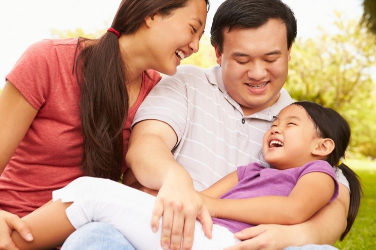 Laughing Mother and father hold their daughter in their lap.