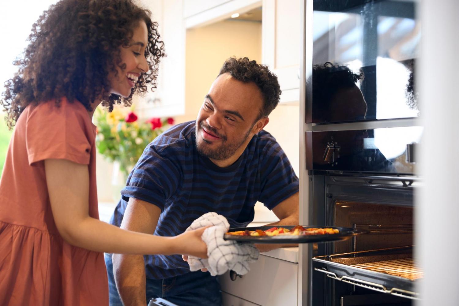 Male and female carer removing pizza from oven