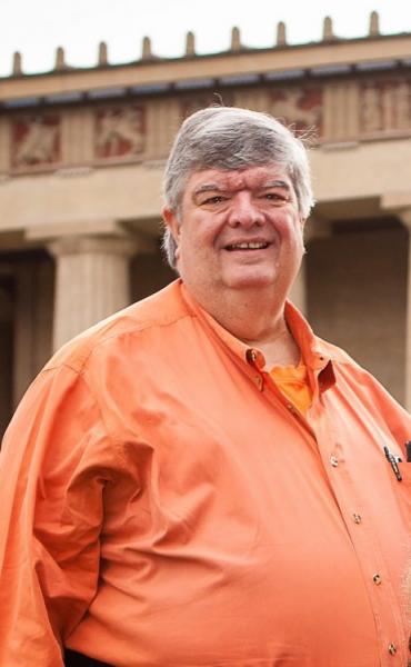 Portrait shot of the late Rob Sasser standing and smiling outside, wearing an orange shirt