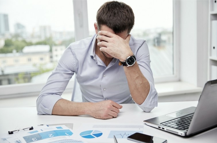 Upset man sits at his desk with his face resting in his hand