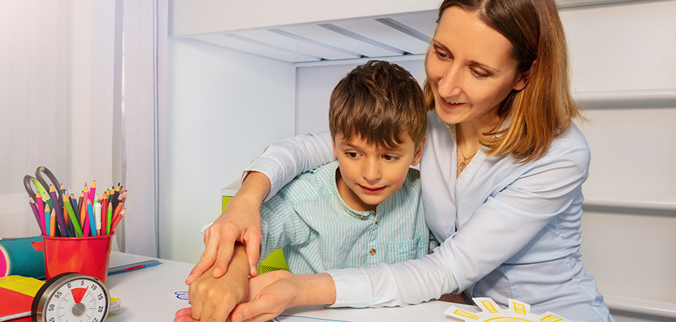 A mum leaning over her child's should helping him with occupational therapy