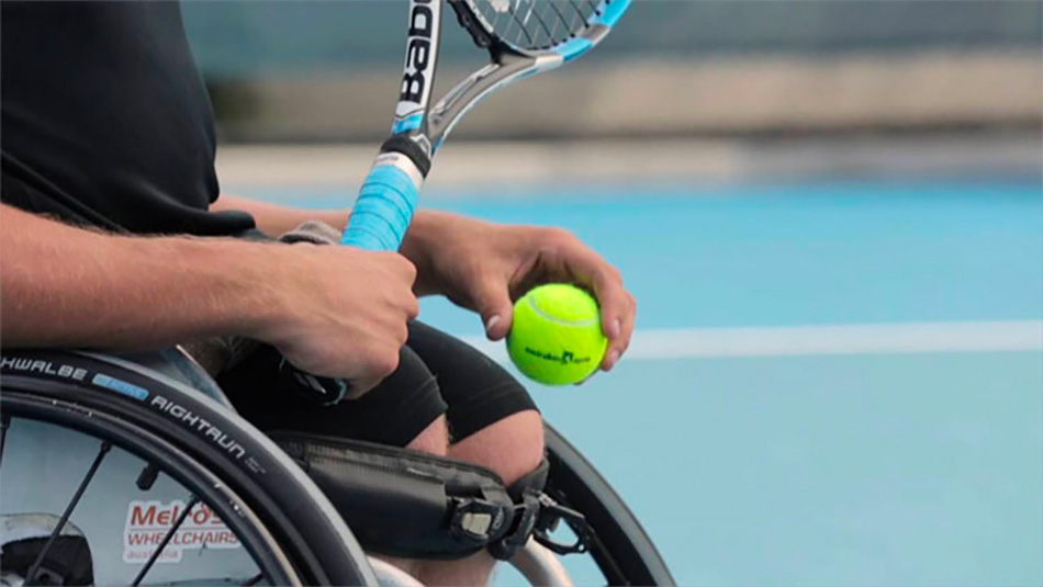 Person in a wheelchair holding a tennis racket and ball