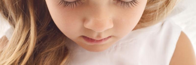 Closeup of a little girls face. She is wearing a white shirt, and her eyes are closed as if in prayer