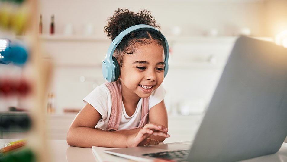 Young girl working on a laptop and smiling. She is wearing headphones.