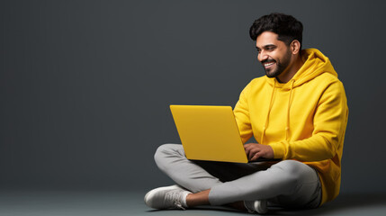 A man in yellow sitting with a laptop on his lap