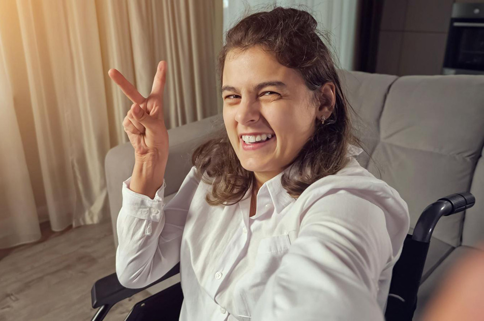 Smiling woman seated in wheelchair in her displaying victory sign with fingers