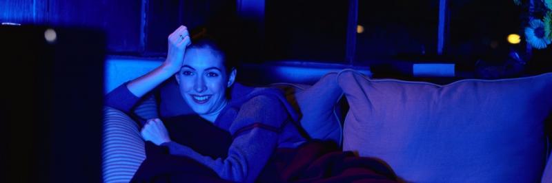 woman sits on couch watching tv, which casts a blue glow in the room