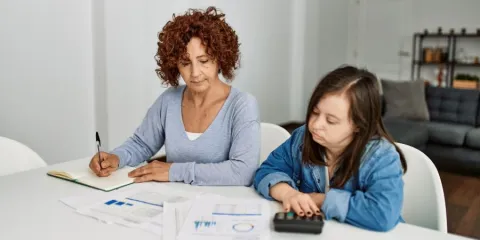 Woman and NDIS participant reviewing paperwork and using a mycarespace budget calculator together at home.