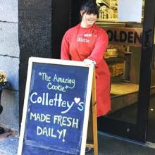 Collete Divitto standing by a welcome sign in front of her bakery