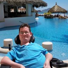 Jon Morrow sits outside smiling in a tropical villa in front of a pool