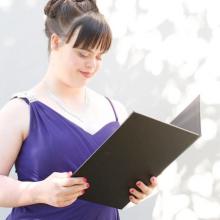 Olivia stands in a purple formal dress, speaking from a folder