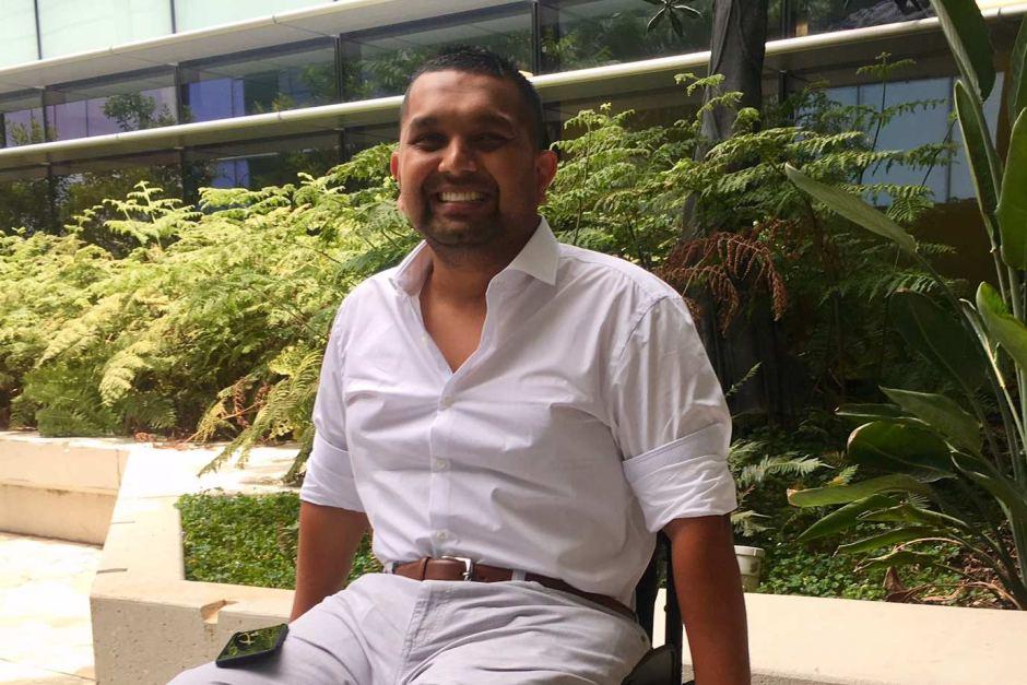 Dinesh Palipana sitting outside and smiling proudly