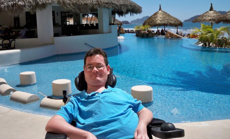 Jon Morrow sits outside smiling in a tropical villa in front of a pool