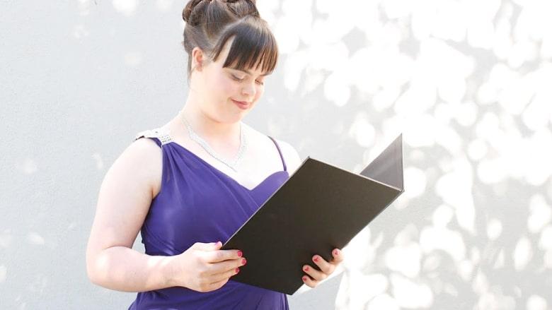 Olivia stands in a purple formal dress, speaking from a folder