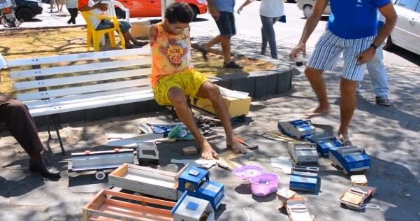 Geraldo Pereira sitting outside in public on a bench, where he builds his toys 