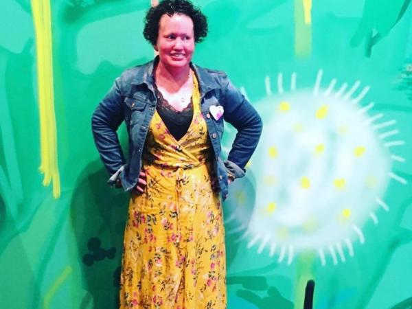 Carly posing, wearing a yellow dress and jean jacket