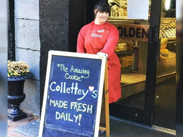 Collete Divitto standing by a welcome sign in front of her bakery