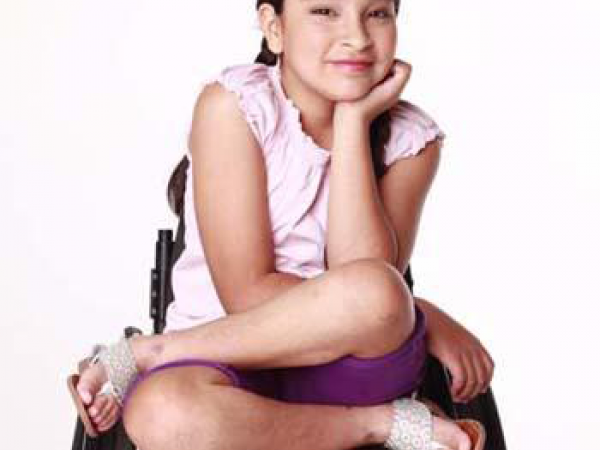 lourdes sits cross legged in her wheelchair and smiles with her face resting in one hand